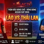 Hình ảnh đồ họa kết hợp cờ và cầu thủ ngôi sao của hai đội tuyển Lào và Thái Lan trước trận đấu vòng bảng ASEAN Cup 2026 trên nền sân vận động.